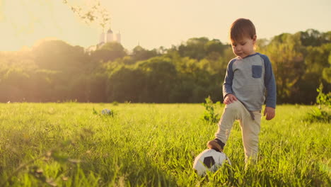 Junge-Steht-Bei-Sonnenuntergang-Mit-Einem-Fußball-Auf-Dem-Gras.
